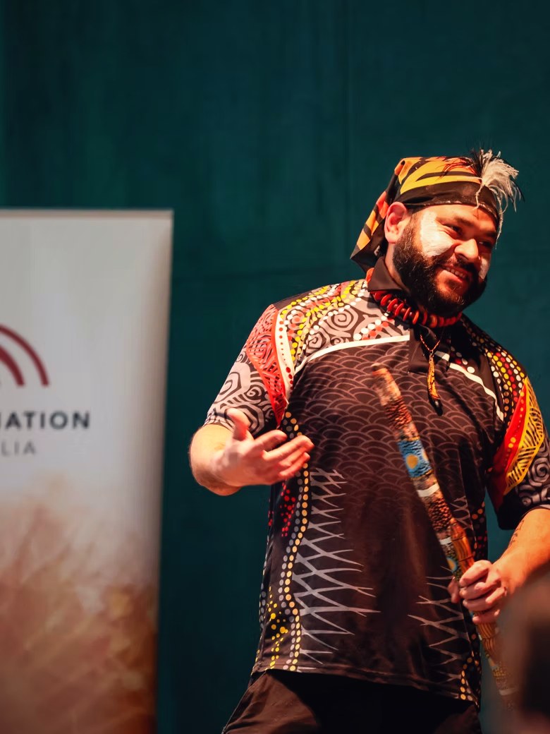 Petiola Wilson performing on stage in cultural dress, holding a yidaki